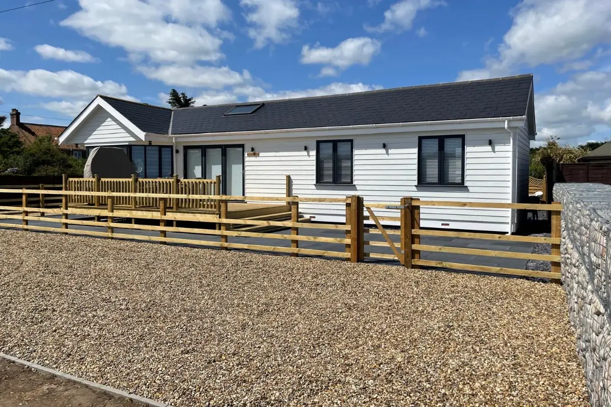 White countryside holiday lodge with gravel driveway, wooden fencing and blue sky