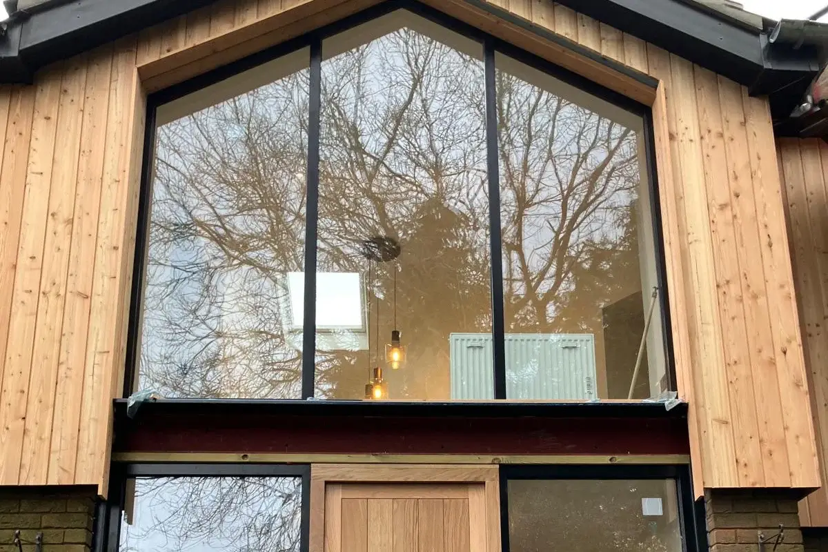 Contemporary entrance with timber door, full height glazing, black frame, and vertical timber cladding
