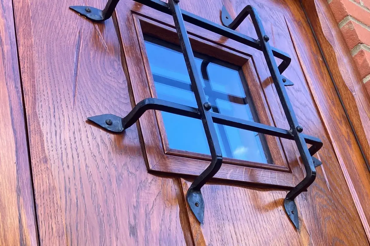 Close-up of a wooden front door with a small glass window and black metal security grille
